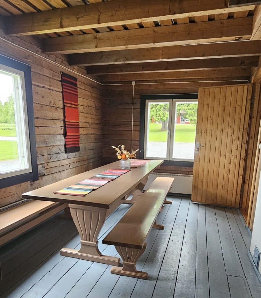 Rustic cabin dining area with a long wooden table and matching benches colorful runners and a small vase of flowers on the table  Kainuun Opisto